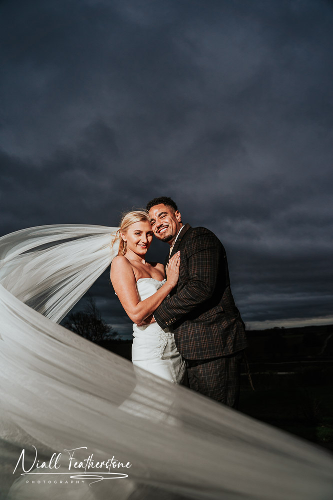 Photo of bride and groom hugging under stormy skys on wedding day