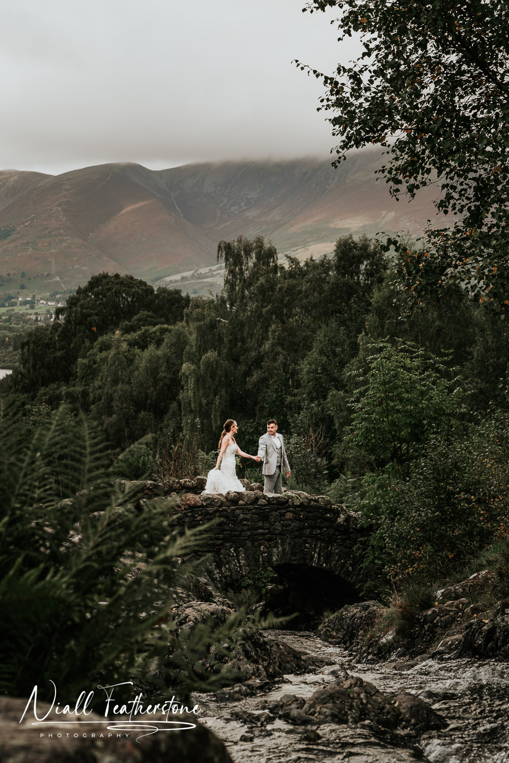 Wedding Couple walking over a bridge in the lake district with mountains in the background